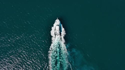Overhead view of motorboat moving at high speed while leaving white wake trail on blue sea surface.