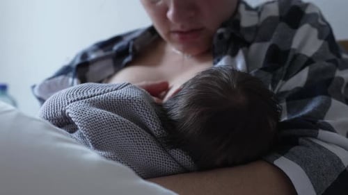 Mother Breastfeeding Newborn Baby in Bed at Home