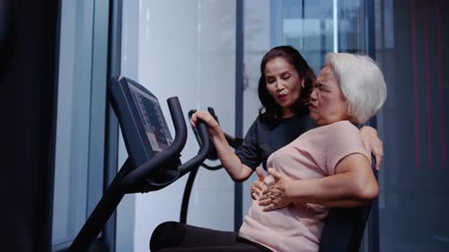 Woman Helping Senior Lady in Gym with Exercise