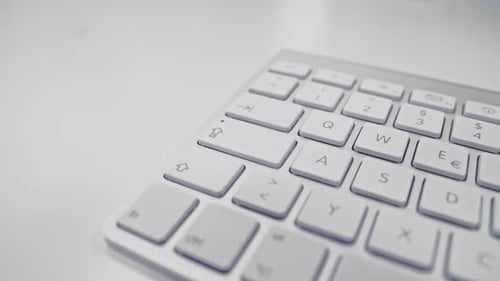 Close shot of a white keyboard. Camera sliding over an apple keyboard on a white desk.