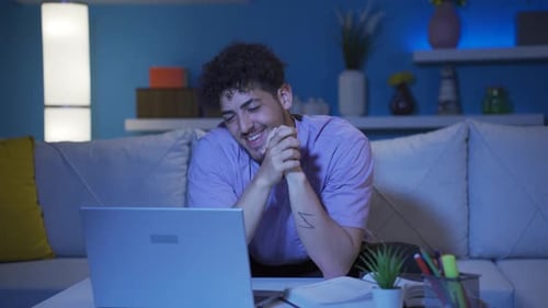 Young Man Happily Chatting on Laptop at Home