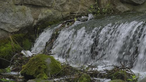 Clear water tumbles over a small fall inside ancient ruins, flowing between moss-covered rocks