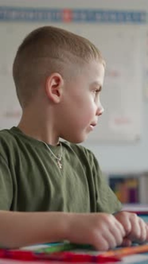 Young Boy with Short Hair and a Green Tshirt Engaged in Classroom Activities Sitting at a Table with