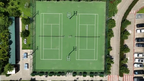 Aerial View Of Green Tennis Courts With Lights, Nets, And Fenced Boundaries Overlooking Parks Nearby