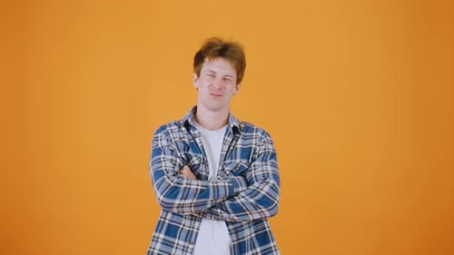 A Man in a Plaid Shirt Stands Against an Orange Background Smiling Warmly at the Camera The Vibrant