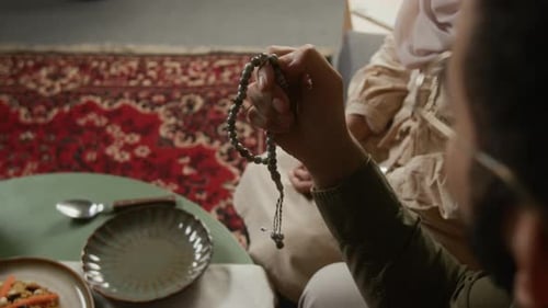 Joven musulmán sosteniendo cuentas de oración y rezando en casa