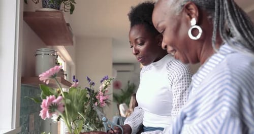 Two women arranging flowers together in kitchen