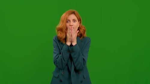 Portrait of young shocked woman holding face looking at camera on green screen chromakey background.