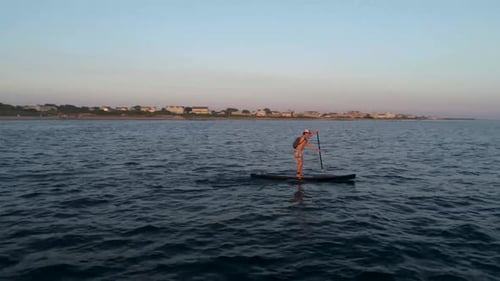 Man Paddle Boarding on Ocean at Sunrise