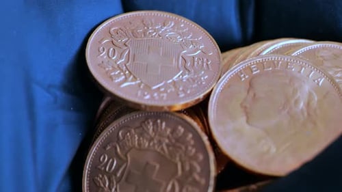 Handheld close up of many golden 20 vreneli francs lighting by sunlight. Helvetia and swiss cross de
