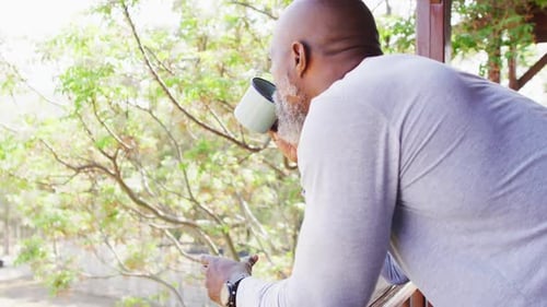 Man Drinks from Mug on Porch Outdoors