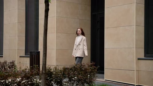 Empresaria que sale de un edificio Una empresaria con un blazer beige sale de un edificio moderno