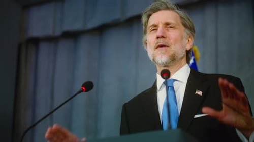 Man Giving Speech at Podium with Microphones