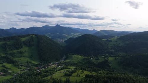 Aerial View of Green Mountain Valley with Forest Hills and Distant Peaks Under Clouds