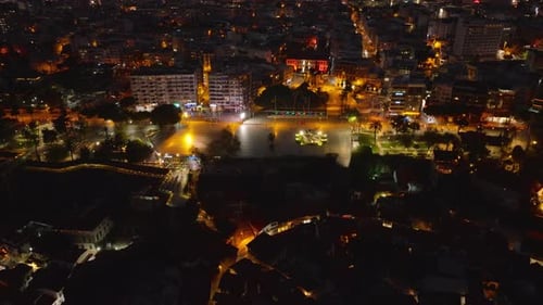 Aerial Shot of Colour Illuminated Square in City Tilt Up Reveal Night Cityscape of Metropolis