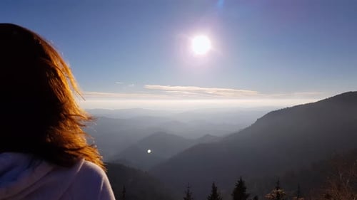 A woman standing on a mountain and looking at a landscape on a windy day