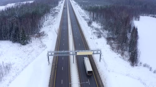 A white truck drives along the road among snowy trees.