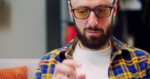 Close Up of Caucasian Man in Glasses Sitting on Couch in Cozy Room at Home and Working on Computer