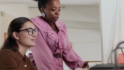 Two Diverse Women Collaborating at Computer in Modern Office Environment