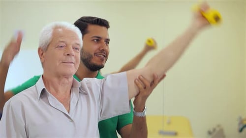 Senior Man Lifts Dumbbell with Assistance in a Hospital Setting