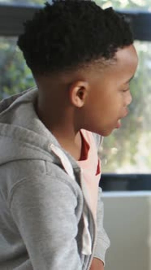 Vertical video: Hearing off-camera voice, student leaning forward, speaking at window desk, hoodie