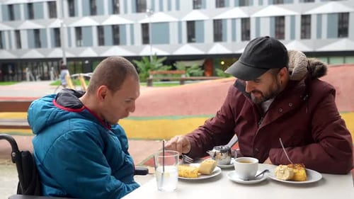 Caregiver feeding disabled man in wheelchair at outdoor cafe