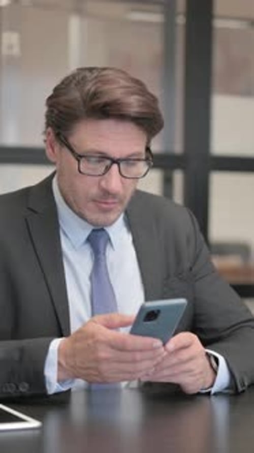 Businessman using Phone while Sitting in Office, vertical