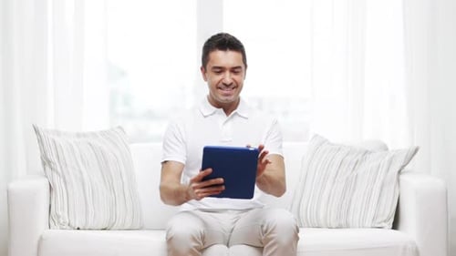 Smiling Man Uses Tablet Device on Couch