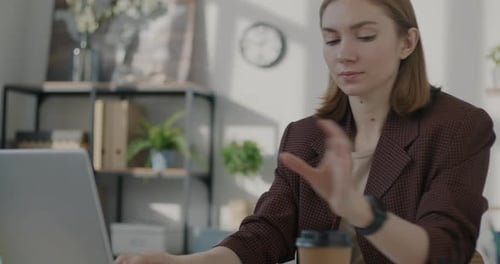 Female Office Worker Using Laptop Working and Drinking to Go Coffee in Workplace