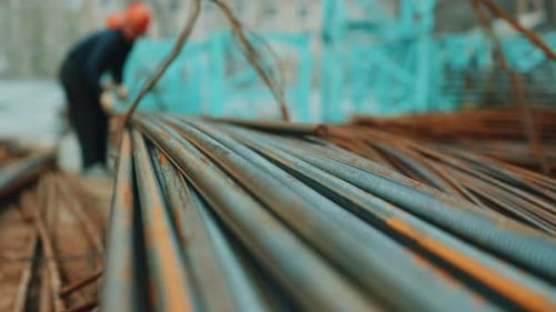 Stack of Steel Rebar Rods with Worker in Background at Construction Site