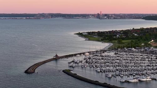 Aerial drone view of a coastal village harbor at sunset with boats docked along piers and calm sea