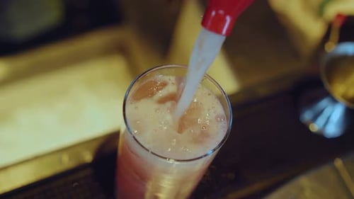 Adding tonic water to the glass with cocktail at the bar. Slow motion.