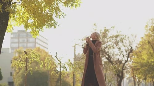 Woman Enjoys Coffee in a City Park in Autumn
