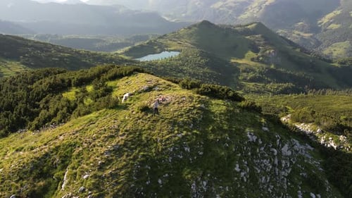 The drone flies over the top of the mountain on which the person is standing. Aerial view.