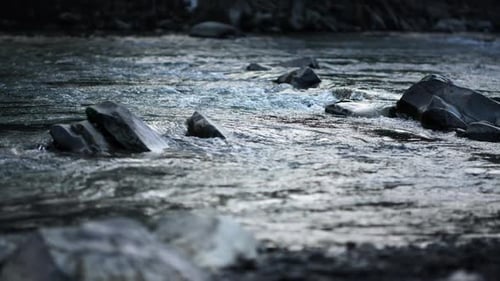 Close up view of fast flowing, turbulent river water rushing past dark rocks