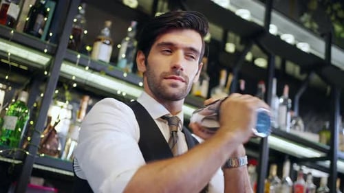 4K Male bartender preparing alcoholic drink in cocktail shaker at restaurant bar.