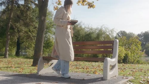 Blonde Woman Reading a Book on a Park Bench Enjoying the Autumn Season