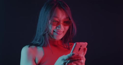 Smiling Woman Using Smartphone in Neon Lighting