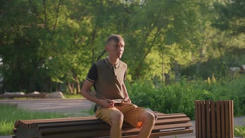 Young Man Sitting on Park Bench, Looking Around