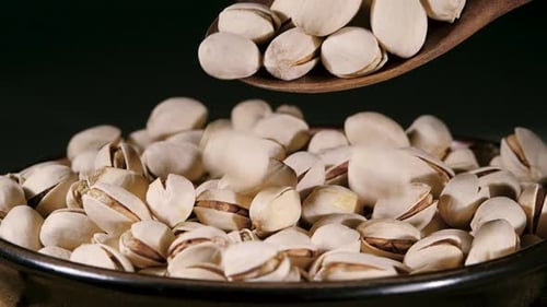 Dried Pistachio Nuts with Cracked Shells and Green Kernels Falling into a Rustic Ceramic Bowl