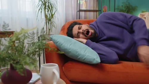Tired Indian Man Lying Down in Bed Taking a Rest at Home Napping Falling Asleep on Sofa Relaxing