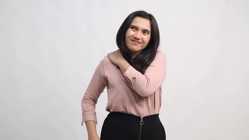 Young woman with a look of discomfort, holding her shoulder as if experiencing pain or stiffness. He