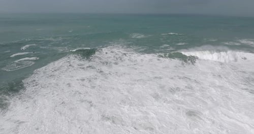 Aerial drone shot of large waves coming into shore on a day with giant waves in Nazaré, Portugal.