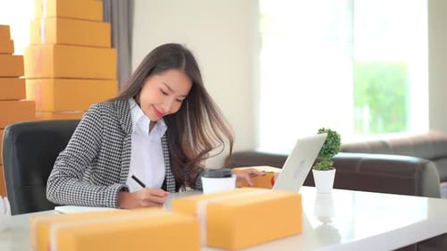 Female worker online store owner using laptop at work preparing parcel boxes checking eCommerce ship