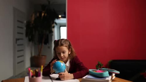 Happy schoolgirl at workplace studying globe in classroom