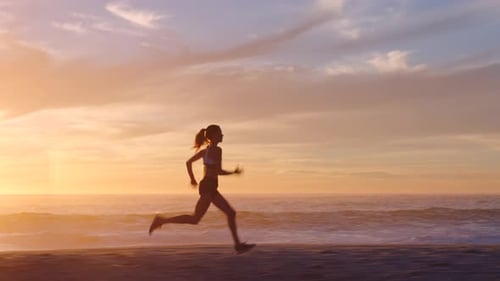 Fit and active jogger running by the ocean and beach shore with sunset sky background