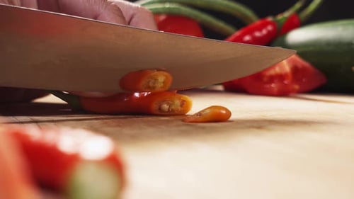 Rote Chilischote mit einem Messer auf einem Holzbrett in Scheiben schneiden