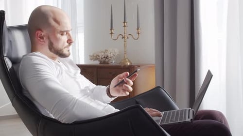 Adult Man Using Laptop and Phone in Chair