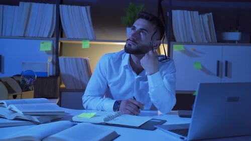 Man Studying and Thinking at Night at Desk