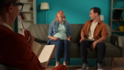 Psychologin macht sich Notizen in einem Notizbuch vor dem Hintergrund eines verschwommenen Paares, das darauf sitzt